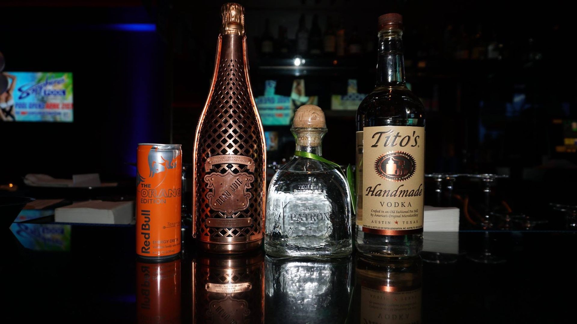 An array of premium spirits including Armand de Brignac, Patrón, and Tito's on a bar, symbolizing the exclusive Bottle Service Experience for Las Vegas clubs tailored for Arizona guests.